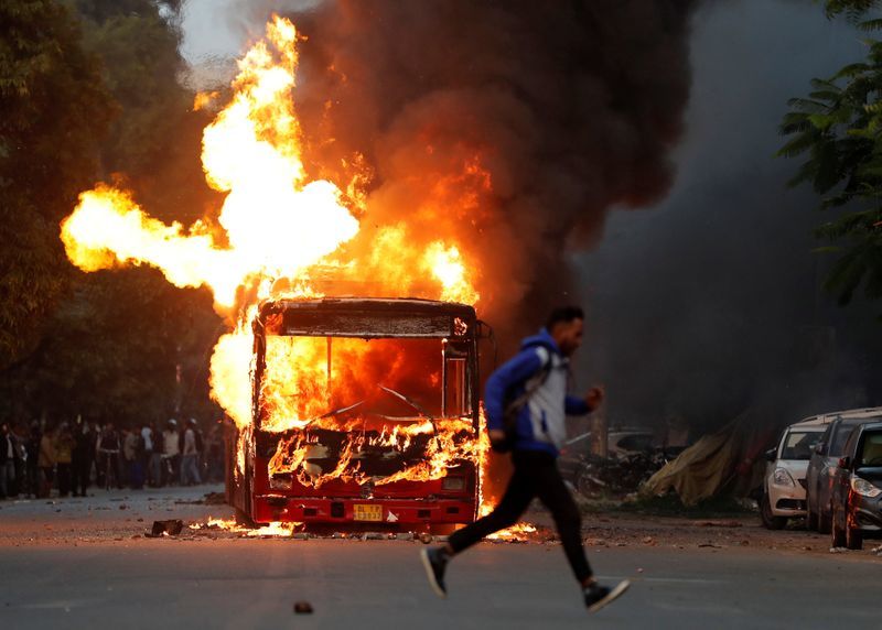 在新德里，抗議新公民法時，一名男子駛過一輛被示威者點燃的燃燒的公共汽車（照片：路透社）