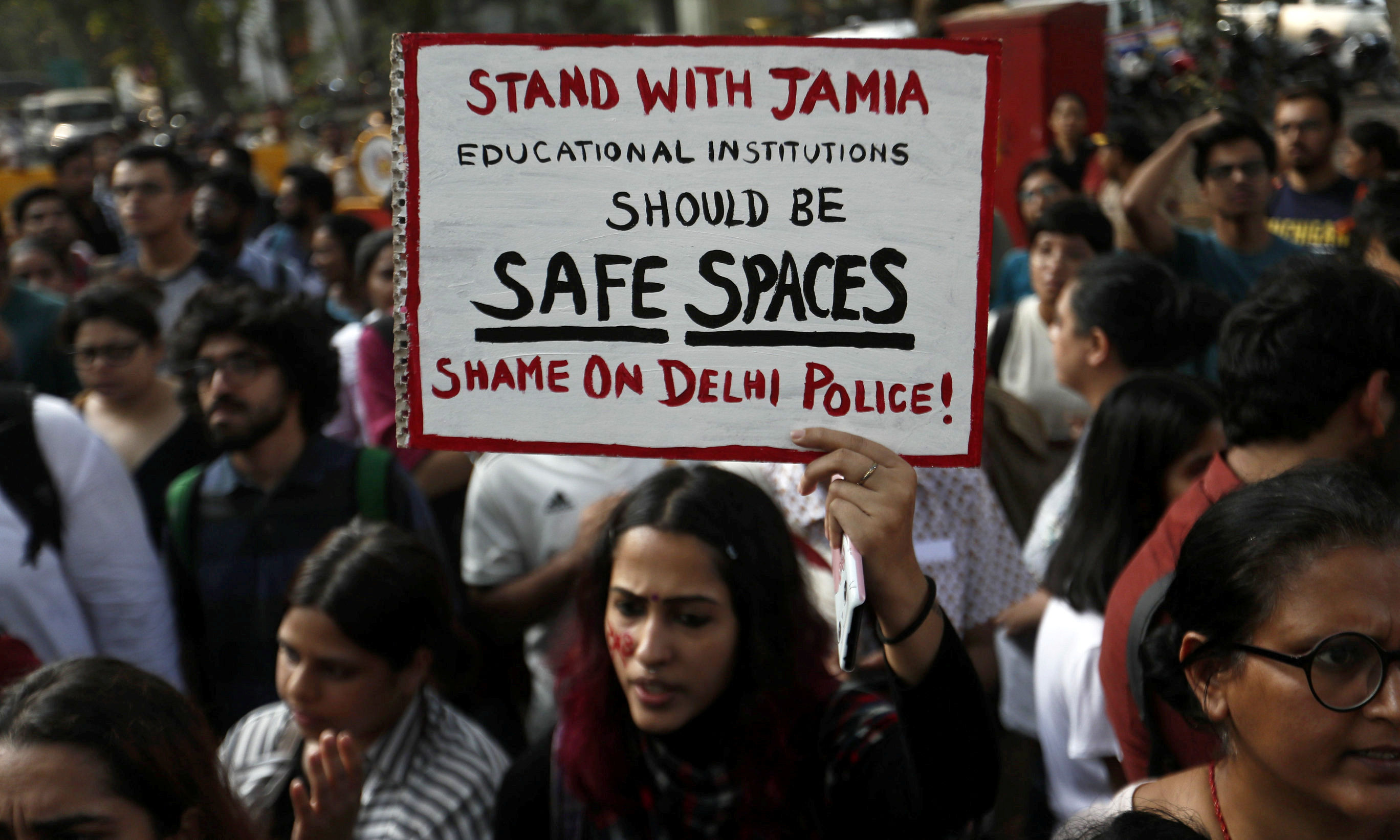在孟買發生抗議新公民法的警察周日進入新德里的校園後，一名婦女與抗議者賈米亞·米莉亞伊斯蘭大學的學生一起舉行標語牌（照片：路透社）