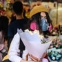 一名男子戴着防护口罩作为预防COVID-19冠状病毒的措施，买了鲜花以纪念情人节